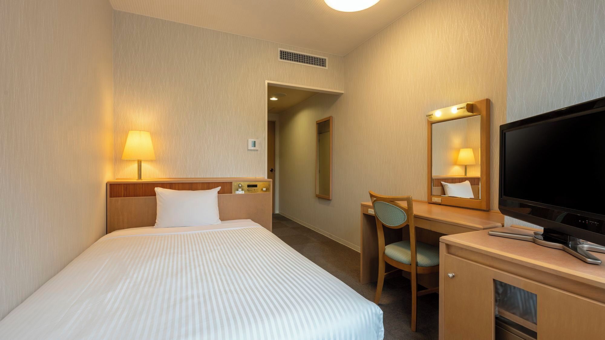 A hotel room with a bed, desk, chair, television, and a mirror.