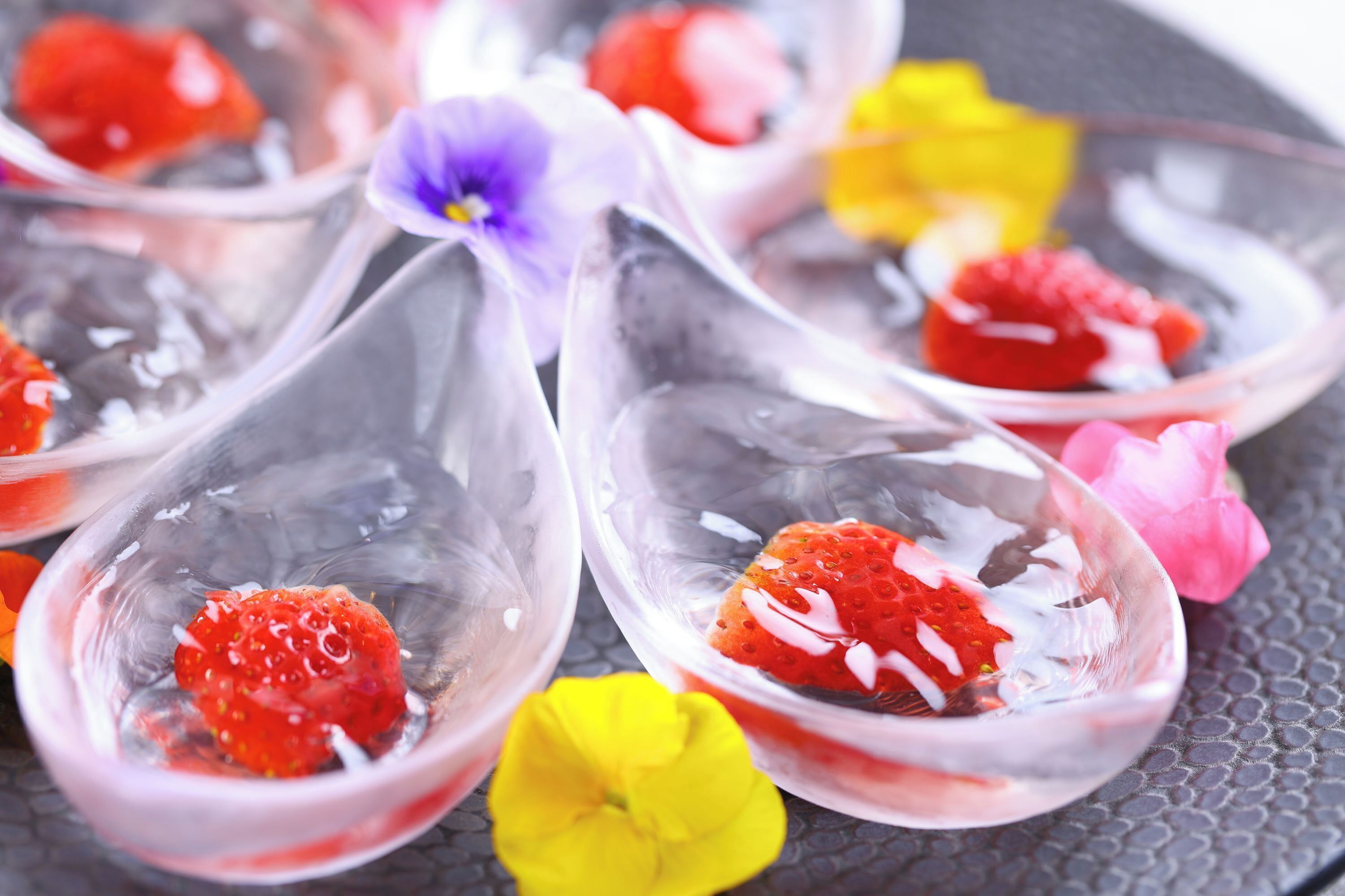 Une vue rapprochée de cuillères en verre transparent remplies de caviar rouge et de crème blanche, entourées de fleurs aux couleurs vives.