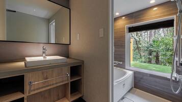 Een moderne badkamer met een grote spiegel, een houten wastafelmeubel, een witte wastafel en een bad met uitzicht op een tuin.