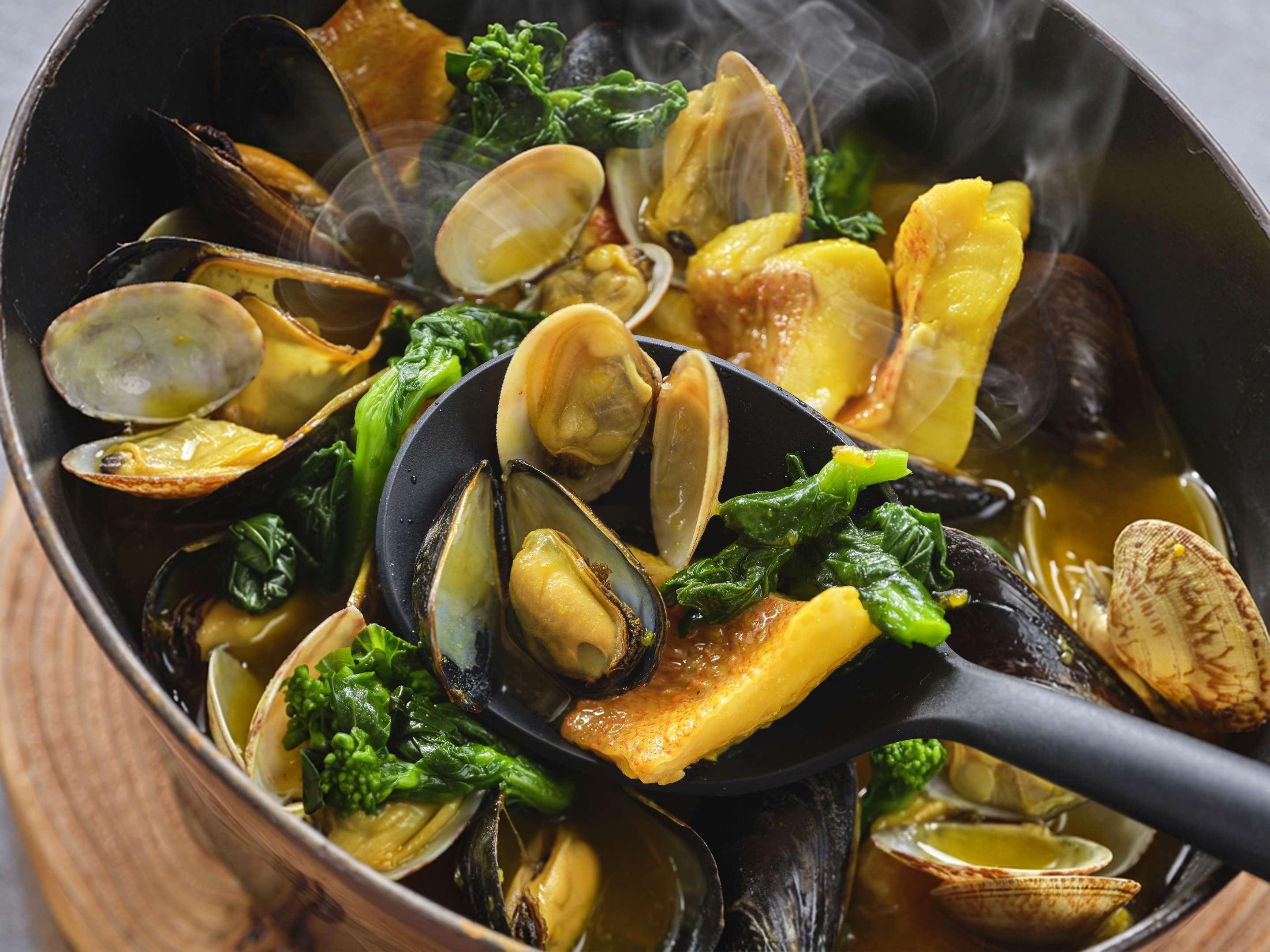 Primer plano de un plato de mariscos con almejas y verduras en una sartén.