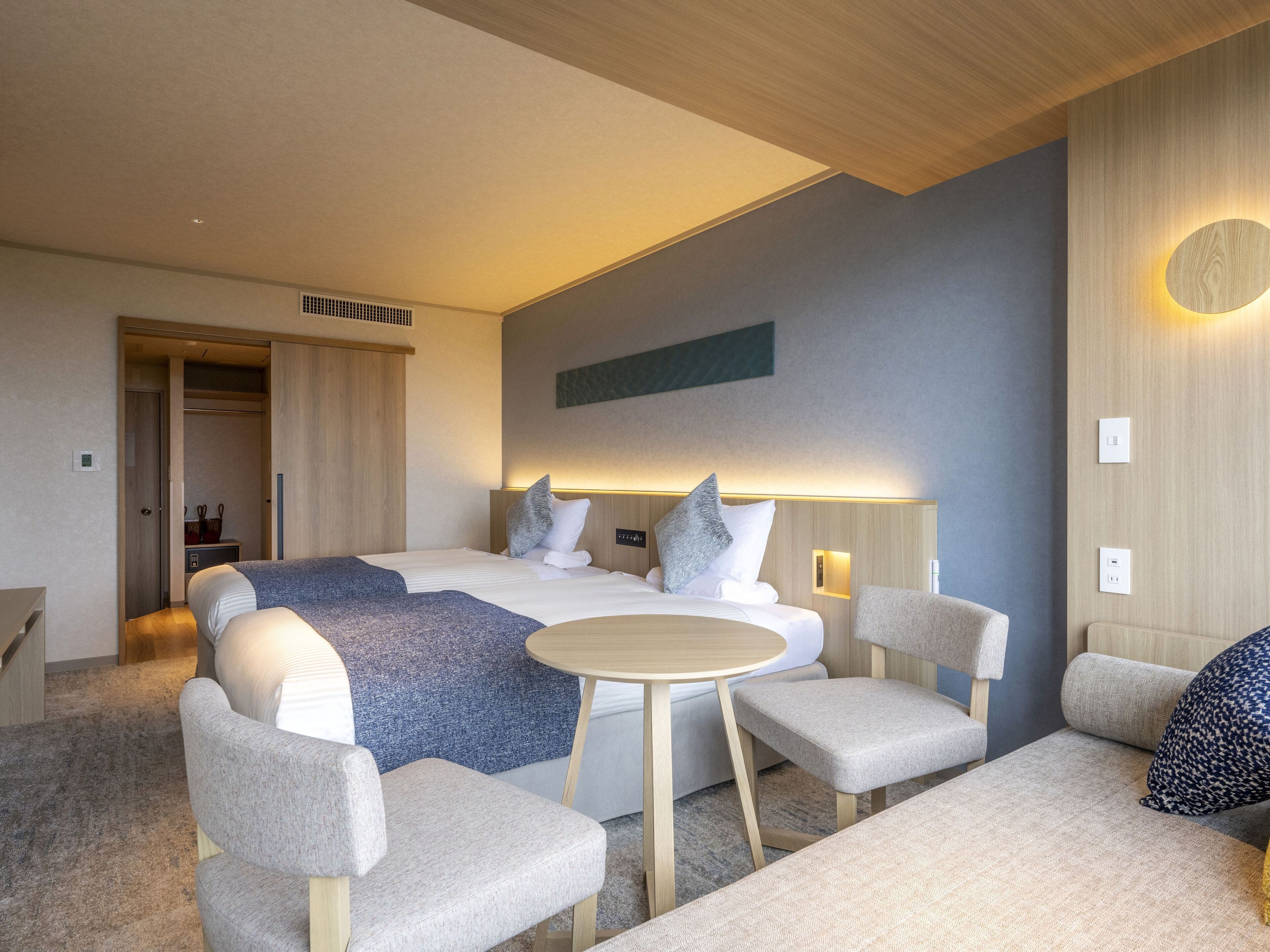 Habitació d'hotel moderna amb un llit gran, dues taules de nit, una taula de cafè rodona i dues butaques.