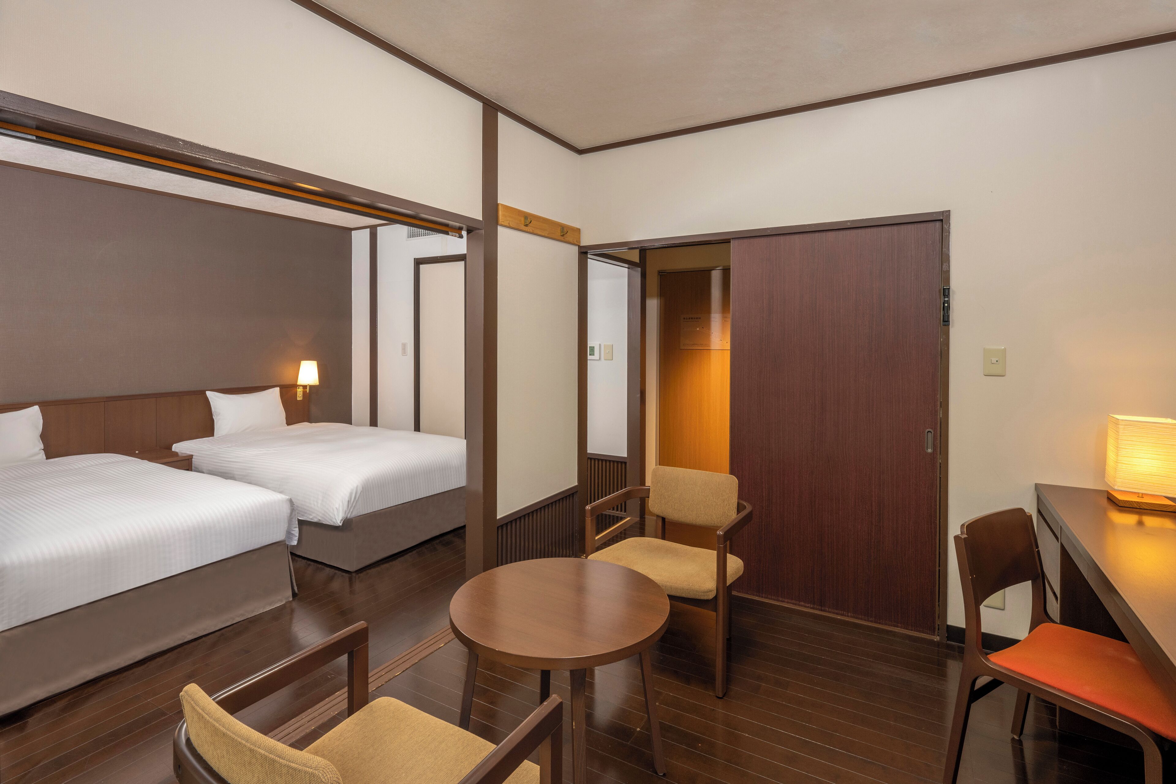 A hotel room with two beds, a small round table, two chairs, and a wooden door.