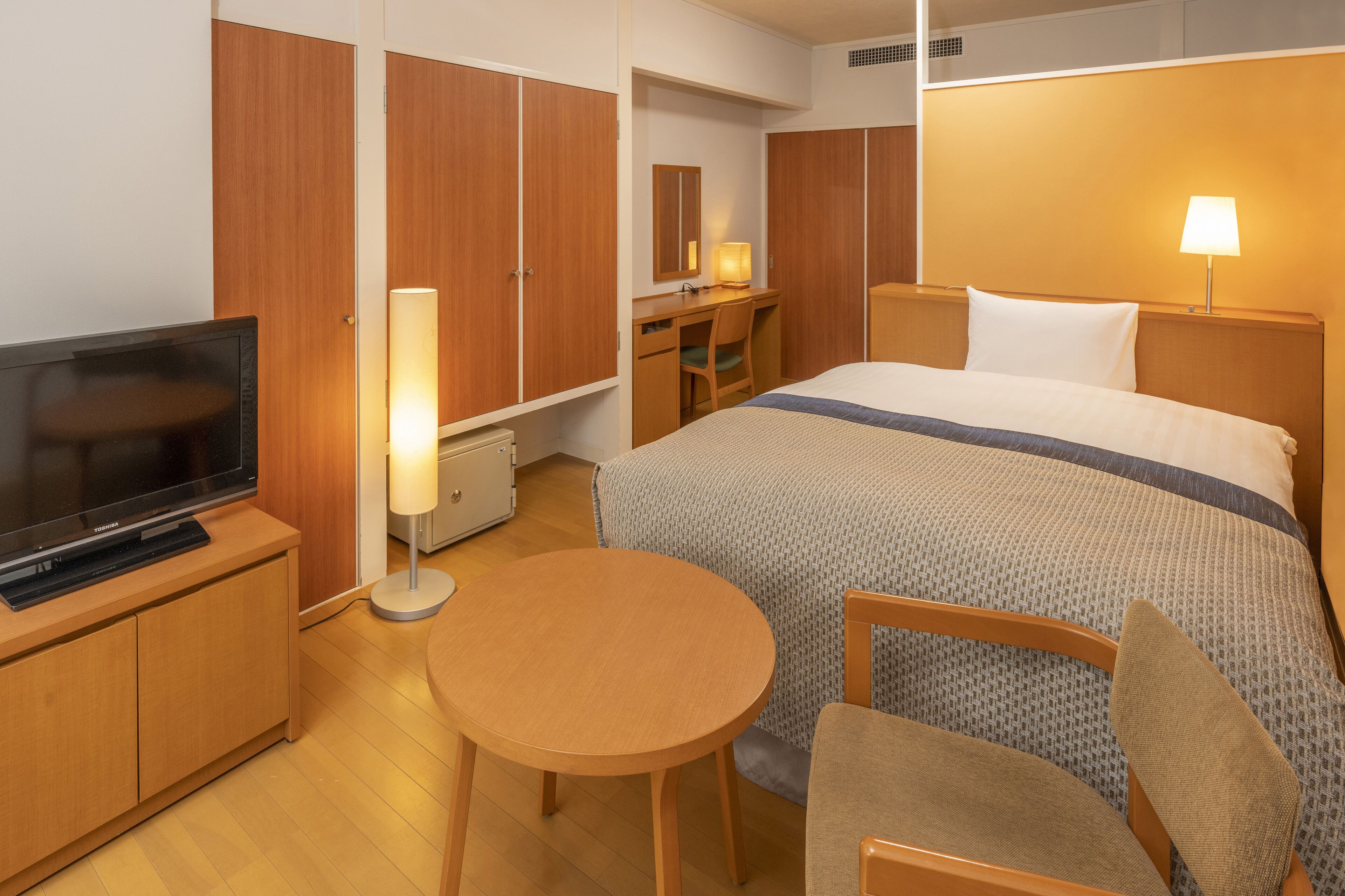A hotel room with a bed, a desk with a chair, a television, and a small round table.