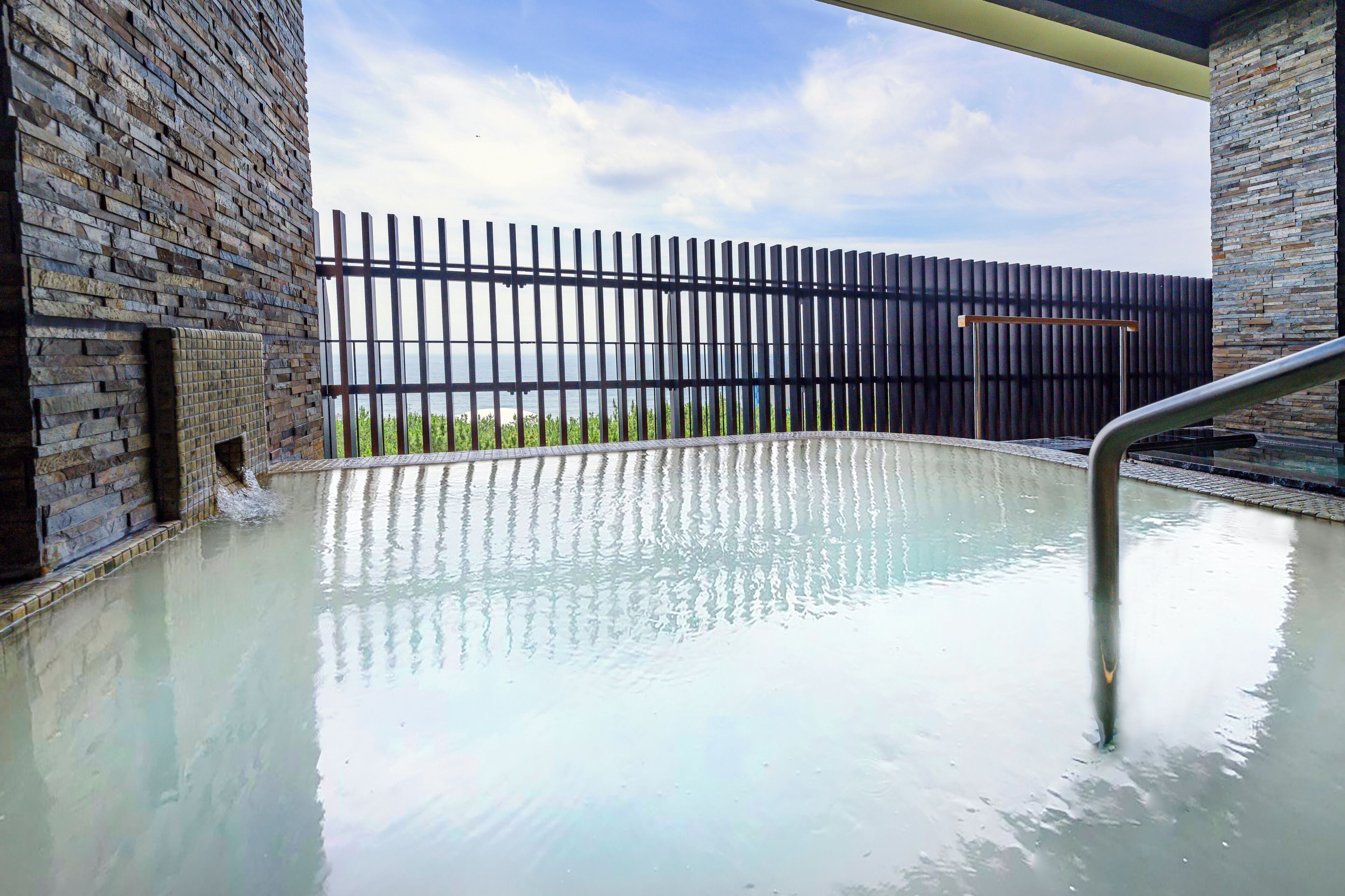 A spa area with a pool, a brick wall, and a view of the sea.