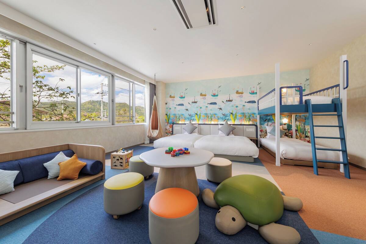 Una sala de juegos para niños con una litera, una mesa redonda llena de juguetes y un mural con escenas marinas.