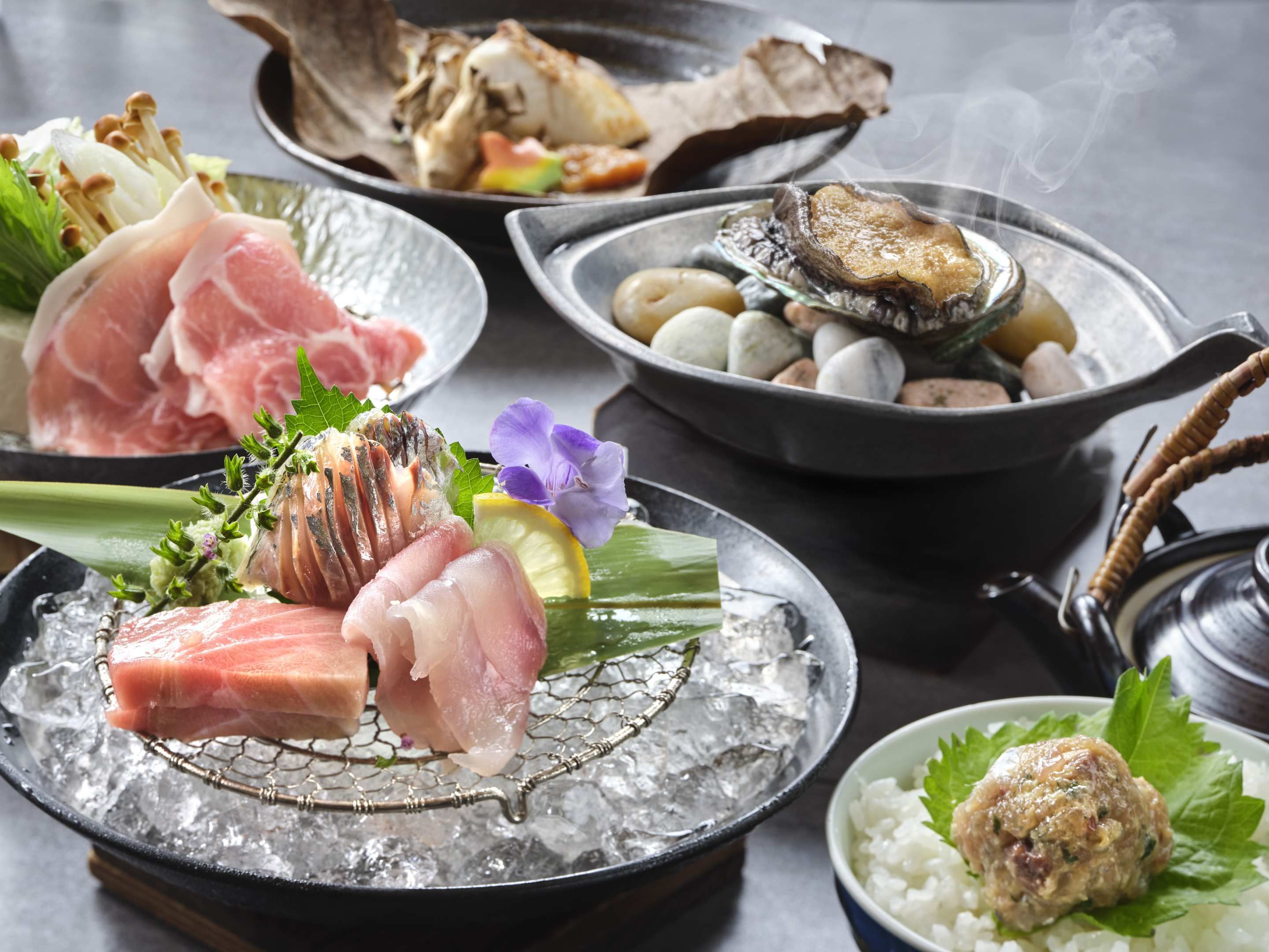 A variety of dishes including sashimi, seafood, and rice, served on a table with ice.