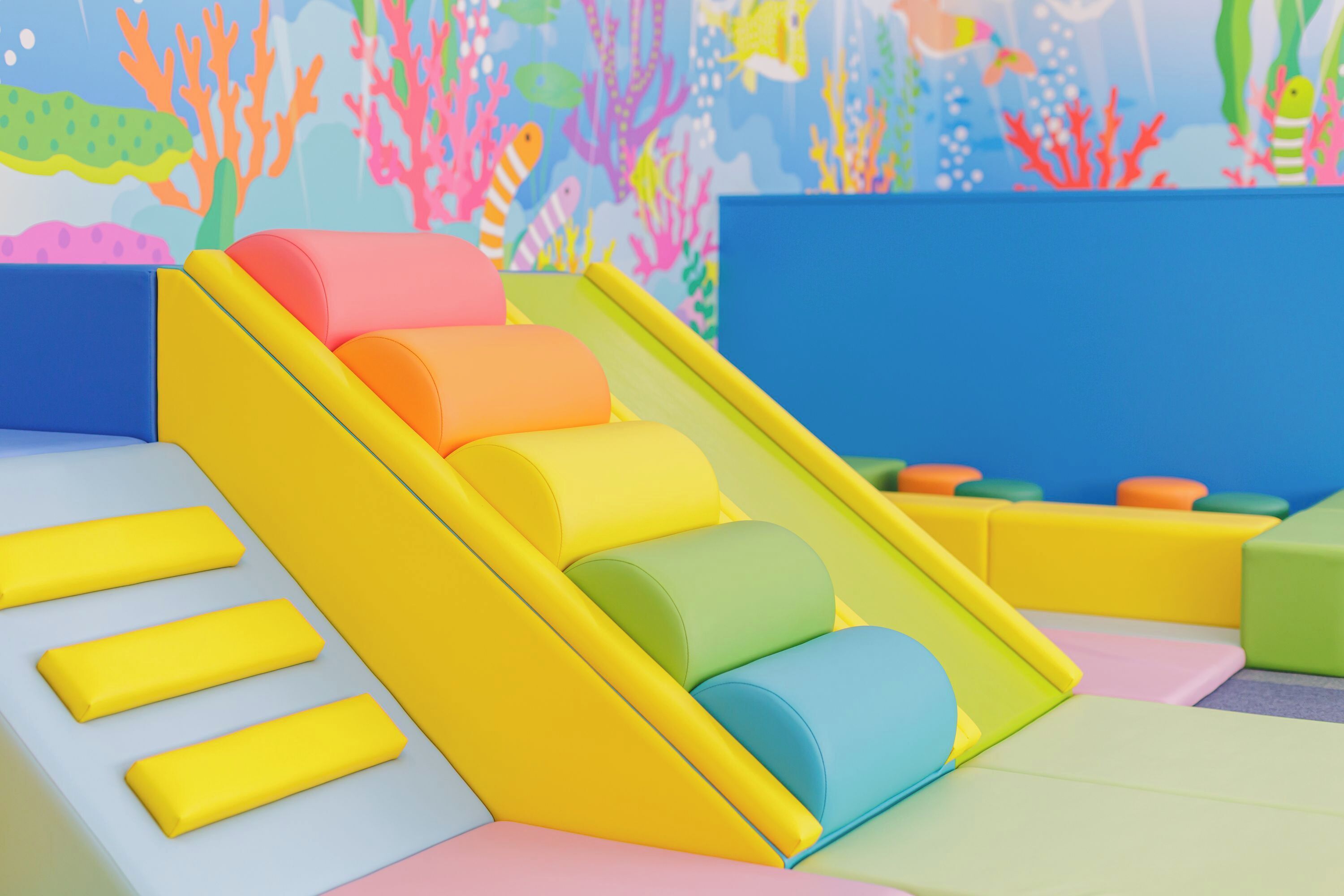 Un área de juegos interior colorida con un tobogán y estructuras de juego blandas.