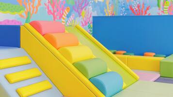Un área de juegos interior colorida con un tobogán y estructuras de juego blandas.