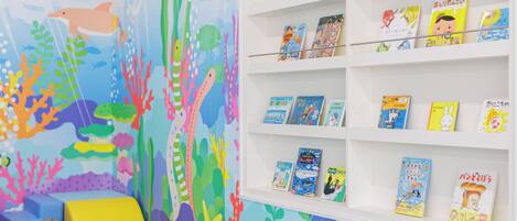 A children's room with a colorful mural of an underwater scene, a white bookshelf with children's books, and a blue cushioned seating area.