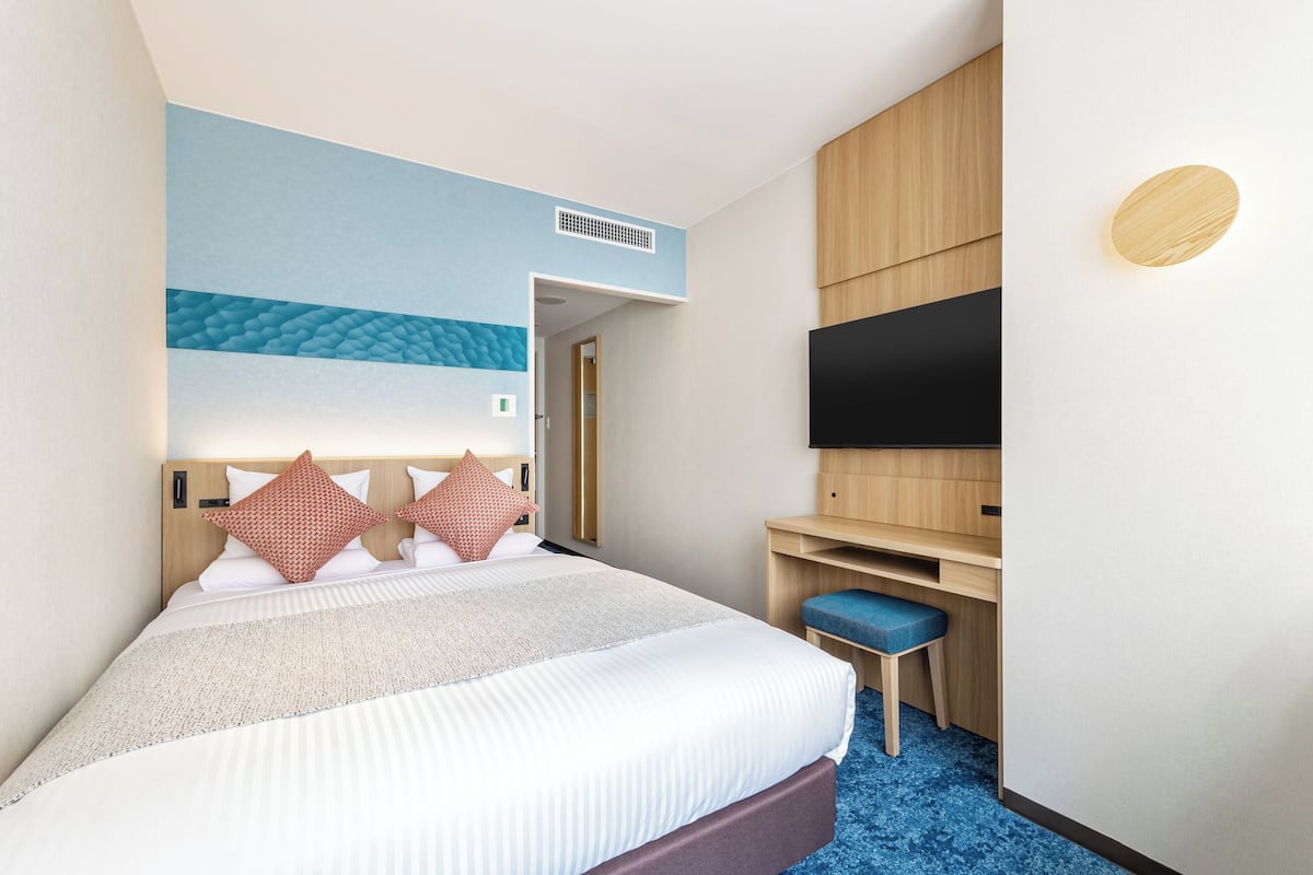 Habitación de hotel con cama, escritorio, silla, televisor y alfombra azul.