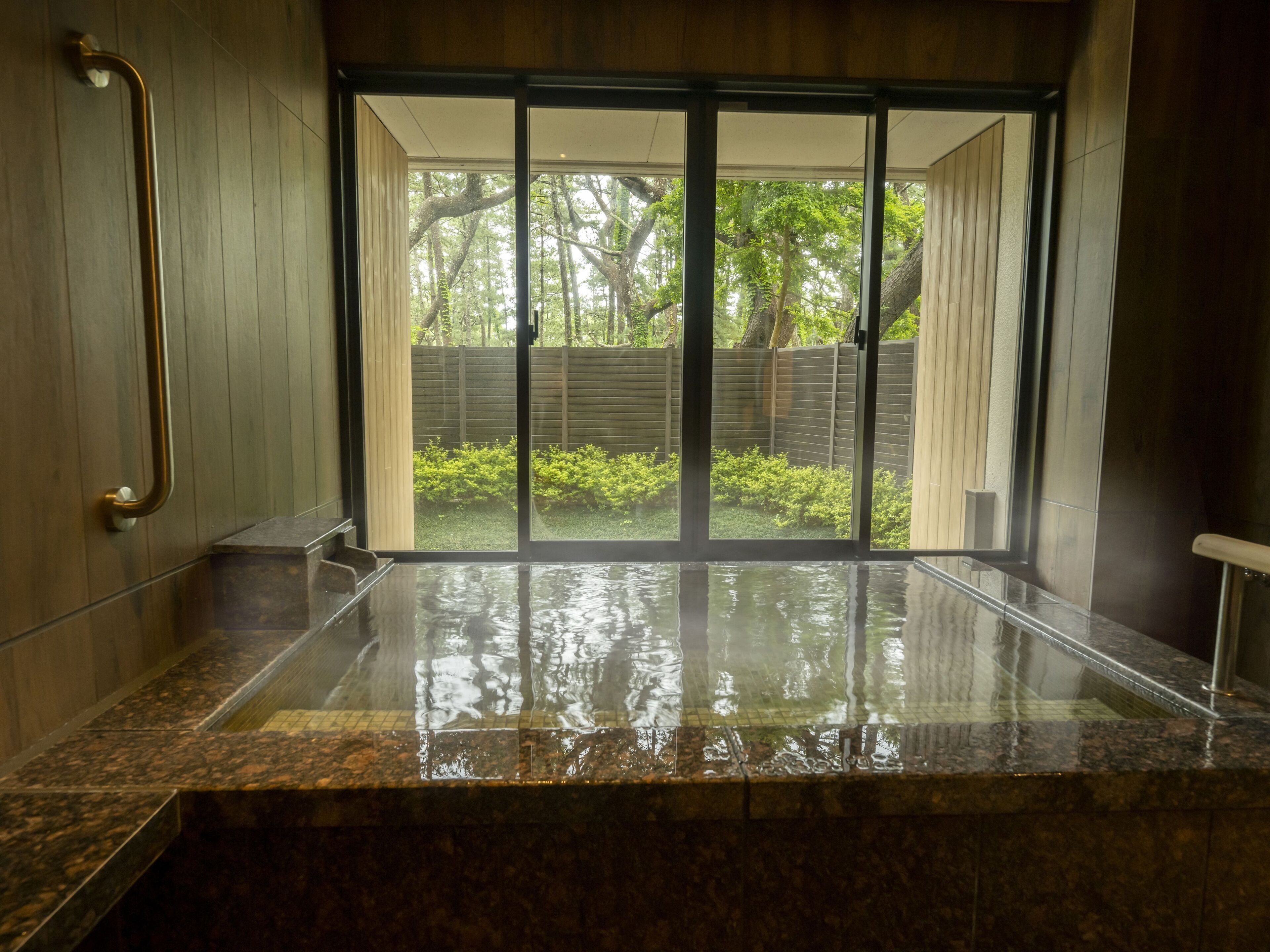 Une salle de bain humide avec une douche en verre, un plancher en bois et une vue sur une cour arrière avec des arbres et des arbustes.