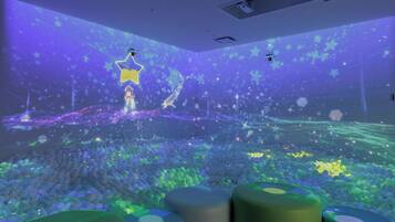 A room with a star projection on the ceiling, a large number of spherical objects on the floor, and cylindrical objects in the foreground.