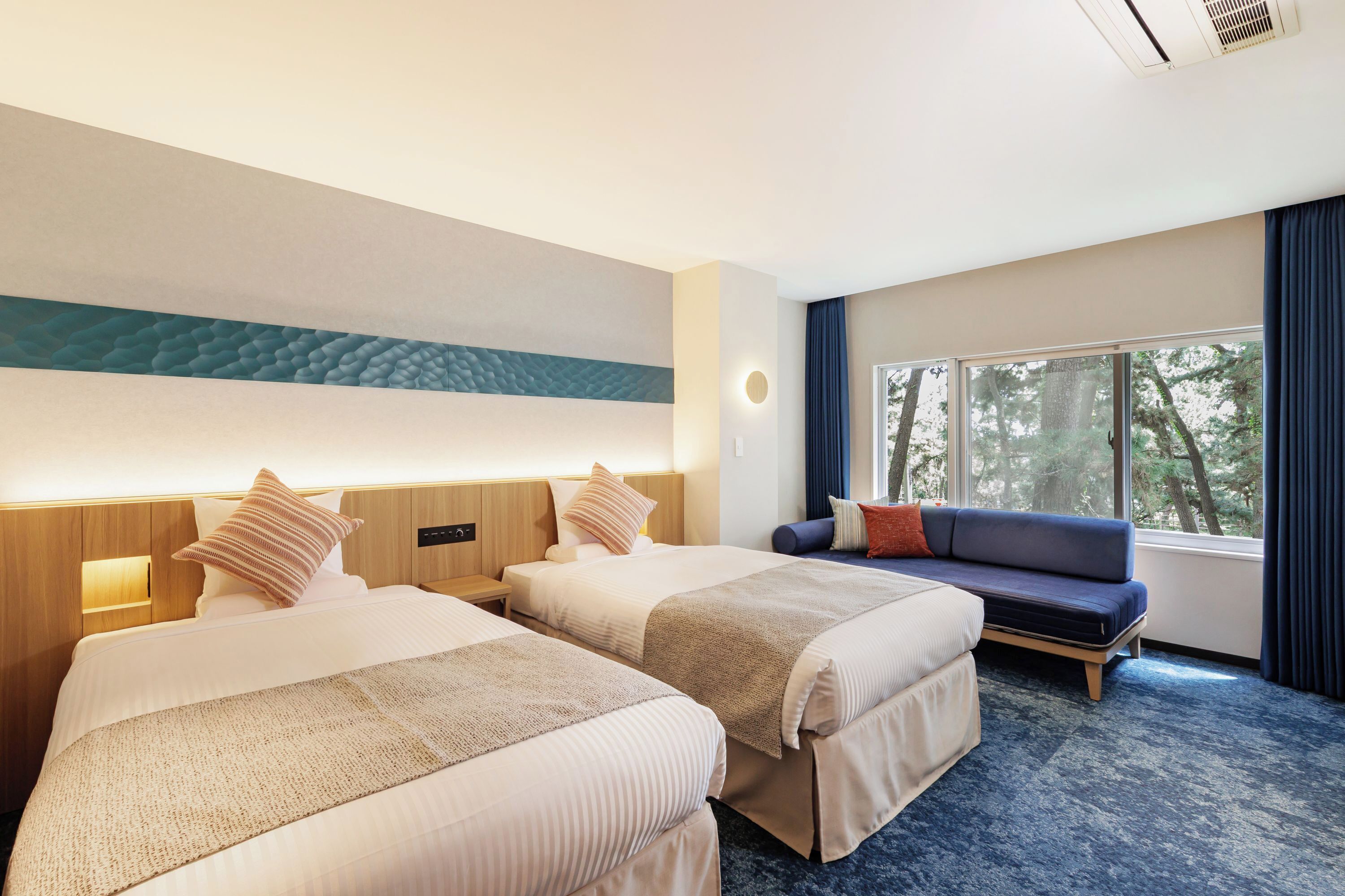 Une chambre d’hôtel avec deux lits, un canapé et une grande fenêtre donnant sur la forêt.
