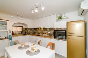 Une cuisine moderne avec des meubles blancs, un réfrigérateur doré et un coin repas comprenant une table et des chaises blanches.