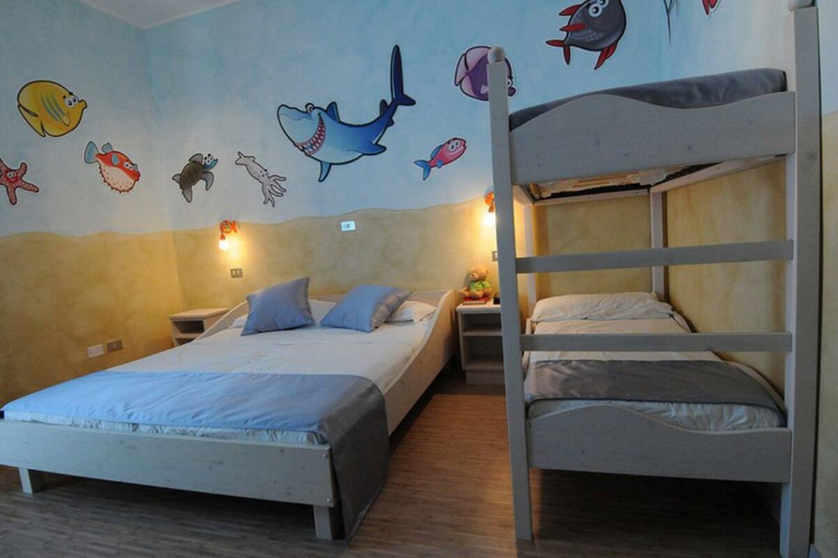 A room with bunk beds, a bed with a blue bedspread, and a wall decorated with fish and sea creatures.