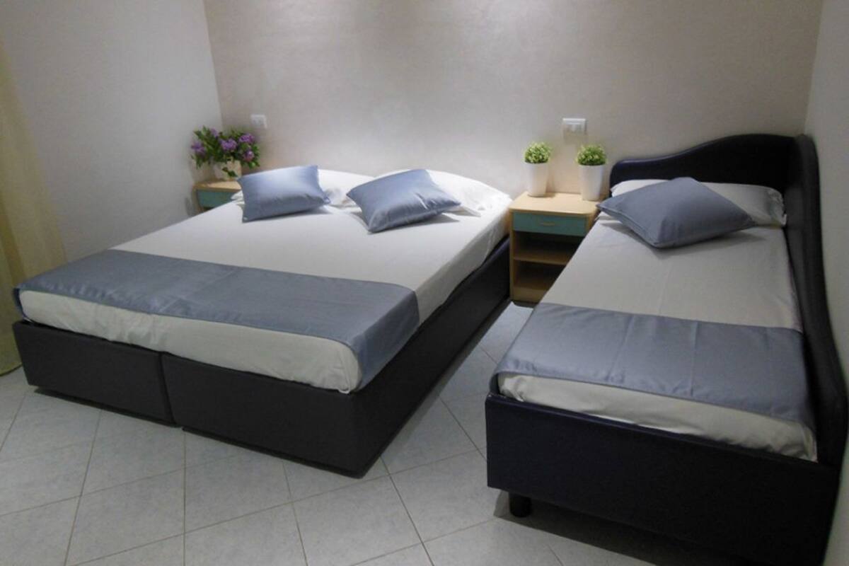 A room with two beds, each with a pillow and a nightstand with a plant.
