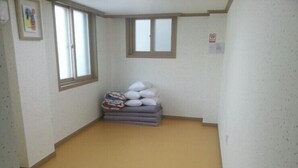 A corner room with a low ceiling, two windows, and a stack of pillows and blankets against the wall. - Jeonju Nangman Sidai Guesthouse - Hostel (Jeonju)