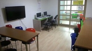 A classroom with a wooden desk, chairs, a television, and computer monitors. - Jeonju Nangman Sidai Guesthouse - Hostel (Jeonju)