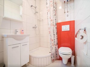Uma casa de banho moderna com uma pia, sanita, chuveiro e uma parede de destaque vermelha.
