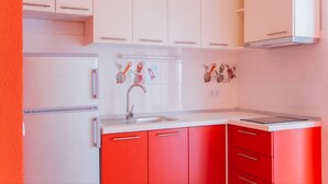 Uma cozinha com armários brancos, bancada vermelha e pia de aço inoxidável.