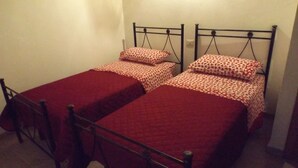 A small, single-room accommodation with two single beds, each with a red bedspread and matching pillows. - Red Cottage Country House (Vico)
