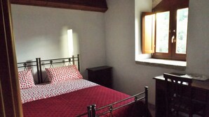 A bedroom with a bed, a nightstand, a desk, and a window with curtains. - Red Cottage Country House (Vico)
