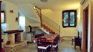 A dining area with a table set for four, a fireplace, a kitchen with a stove, and a staircase leading to another level. - Red Cottage Country House (Vico)