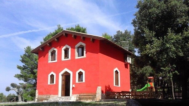 A red building with a central door and multiple windows, surrounded by trees and a playground. - Red Cottage Country House (Vico)