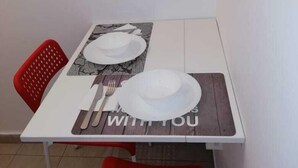 A small dining table with two white plates, a fork, and a knife. There are two red chairs around the table. - Lovely Studio in Omonoia (Athens)
