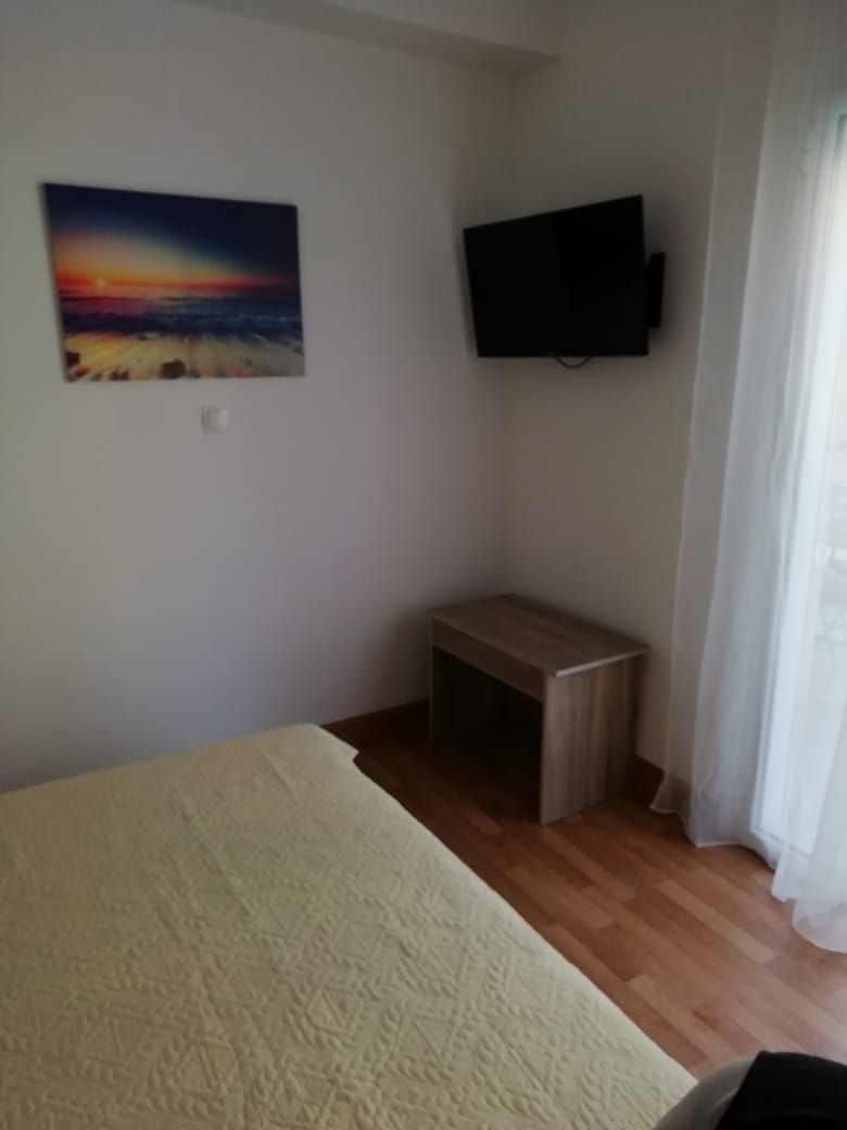 Una habitació amb un llit, una taula de fusta petita, un televisor fixat a la paret i un quadre penjat.