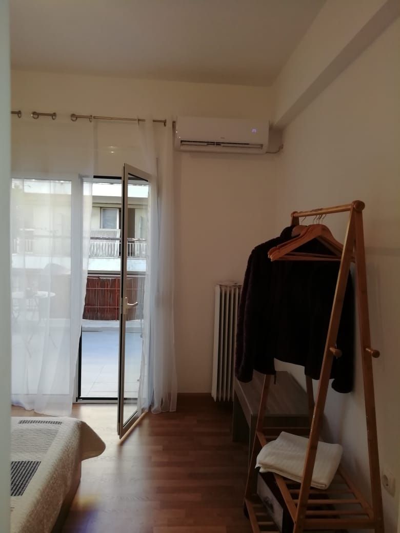 Una habitación con piso de madera, un radiador, un perchero de madera y una ventana con cortinas.