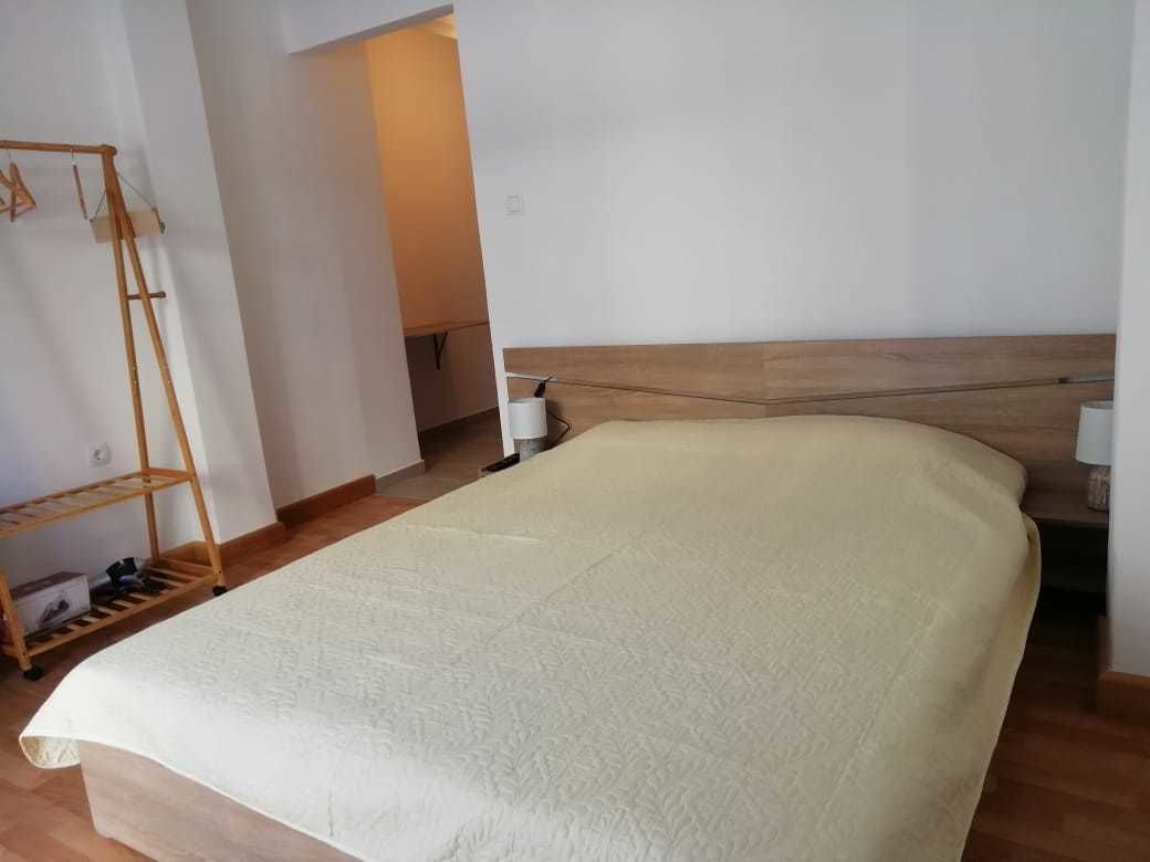 A bedroom with a wooden headboard, a bed with a white duvet, a wooden shelf unit, and a white door in the background.