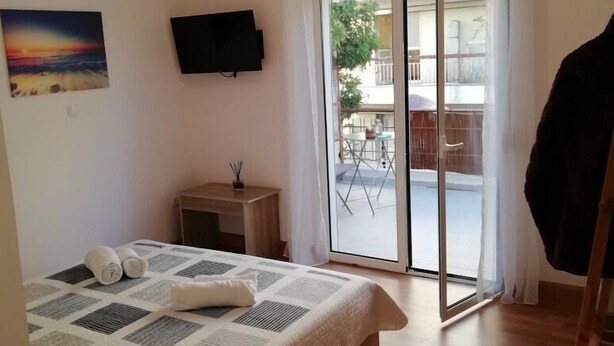 A bedroom with a bed, a TV mounted on the wall, a small table with a plant, and a sliding glass door leading to an outdoor area with a table and chairs. - Lovely Studio in Omonoia (Athens)