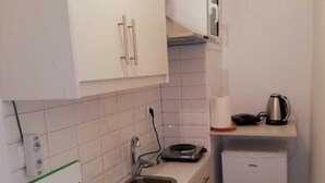 A compact kitchen with white cabinets, a sink, a small refrigerator, and a kettle on the countertop. - Lovely Studio in Omonoia (Athens)
