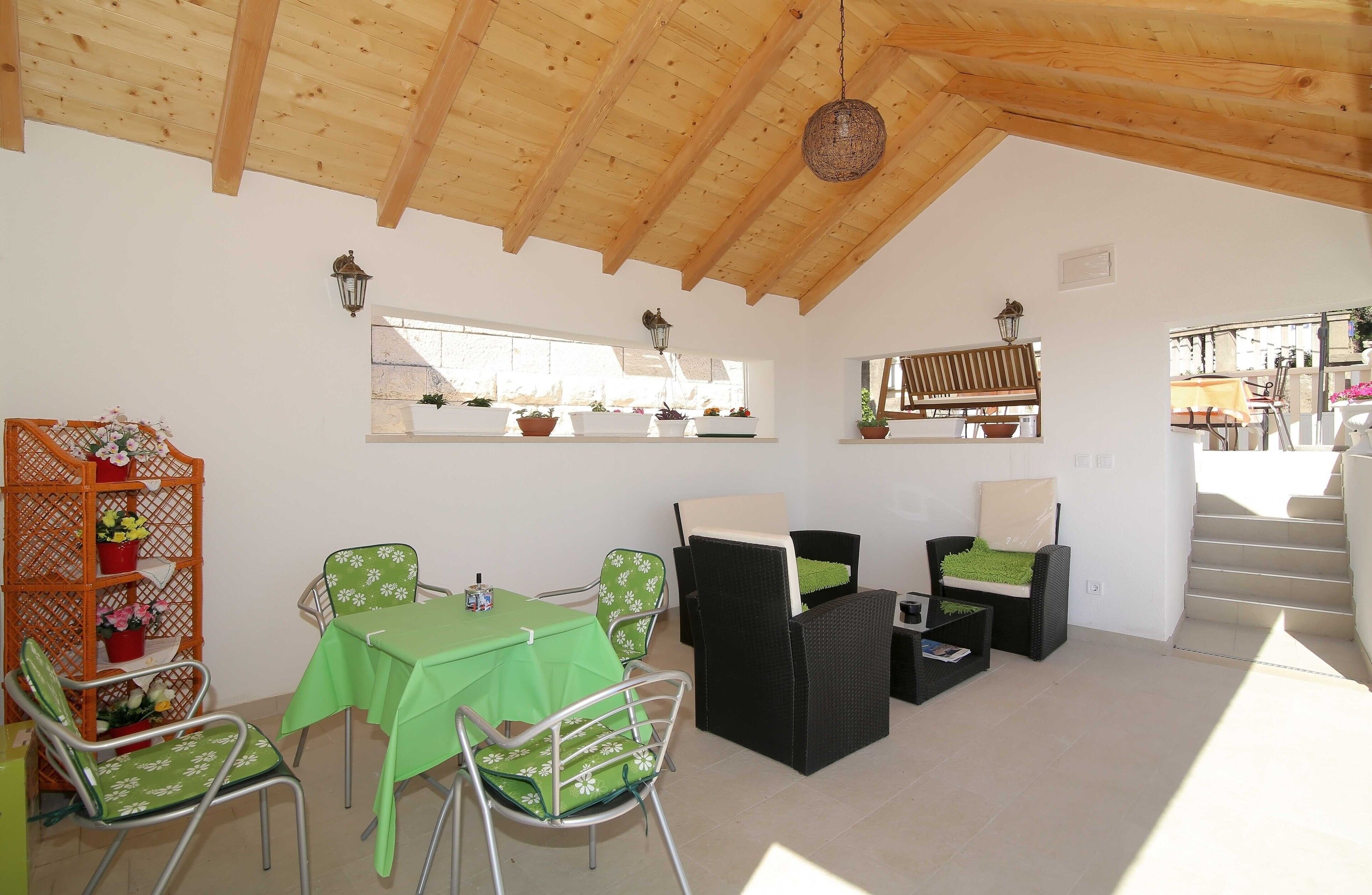 A dining area with a wooden ceiling, green tablecloths, wicker chairs, and a staircase leading to an outdoor area.