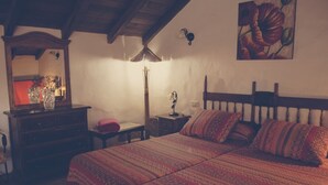 A cozy bedroom with a large bed, a wooden headboard, a nightstand with a lamp, and a dresser with a mirror and vases.
