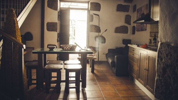 A cozy kitchen with a wooden table, stools, and a stone wall.