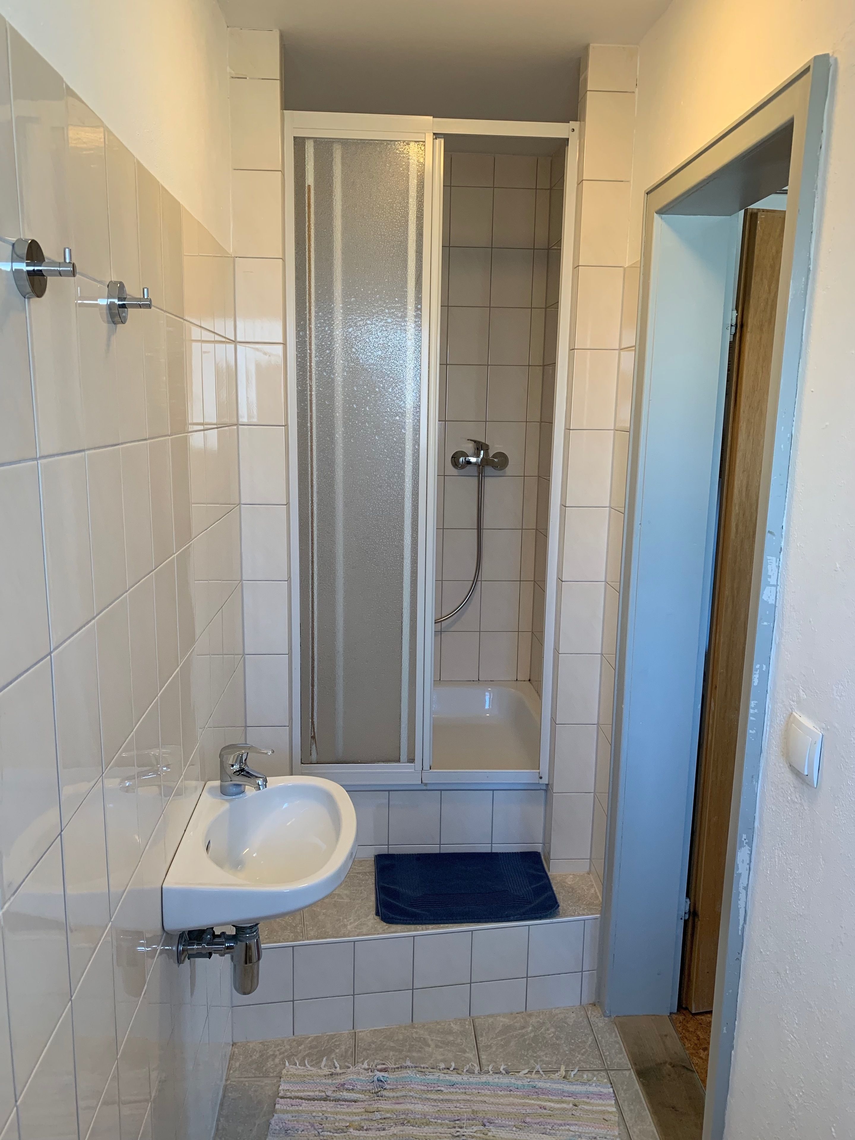 A bathroom with a shower, a sink, and a door leading to another room.