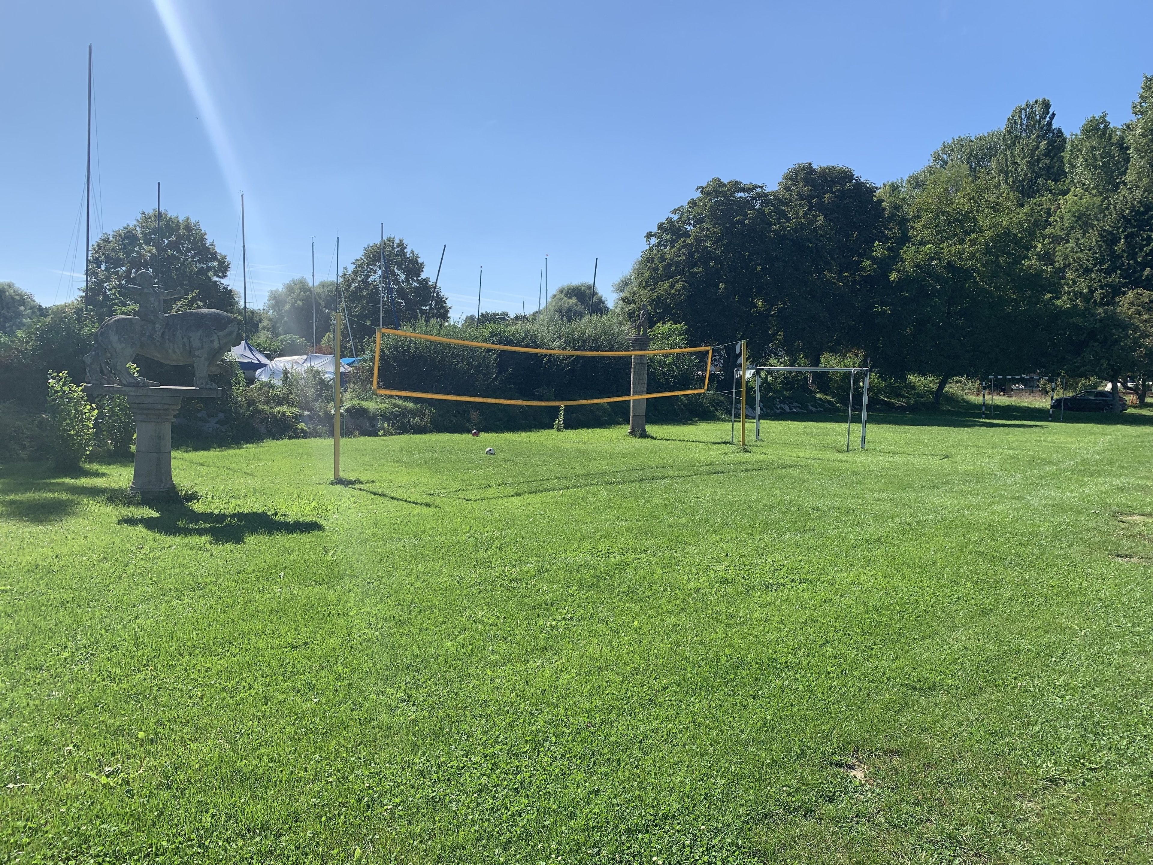 Un filet de volley-ball dans un champ d’herbe, avec des arbres en arrière-plan.