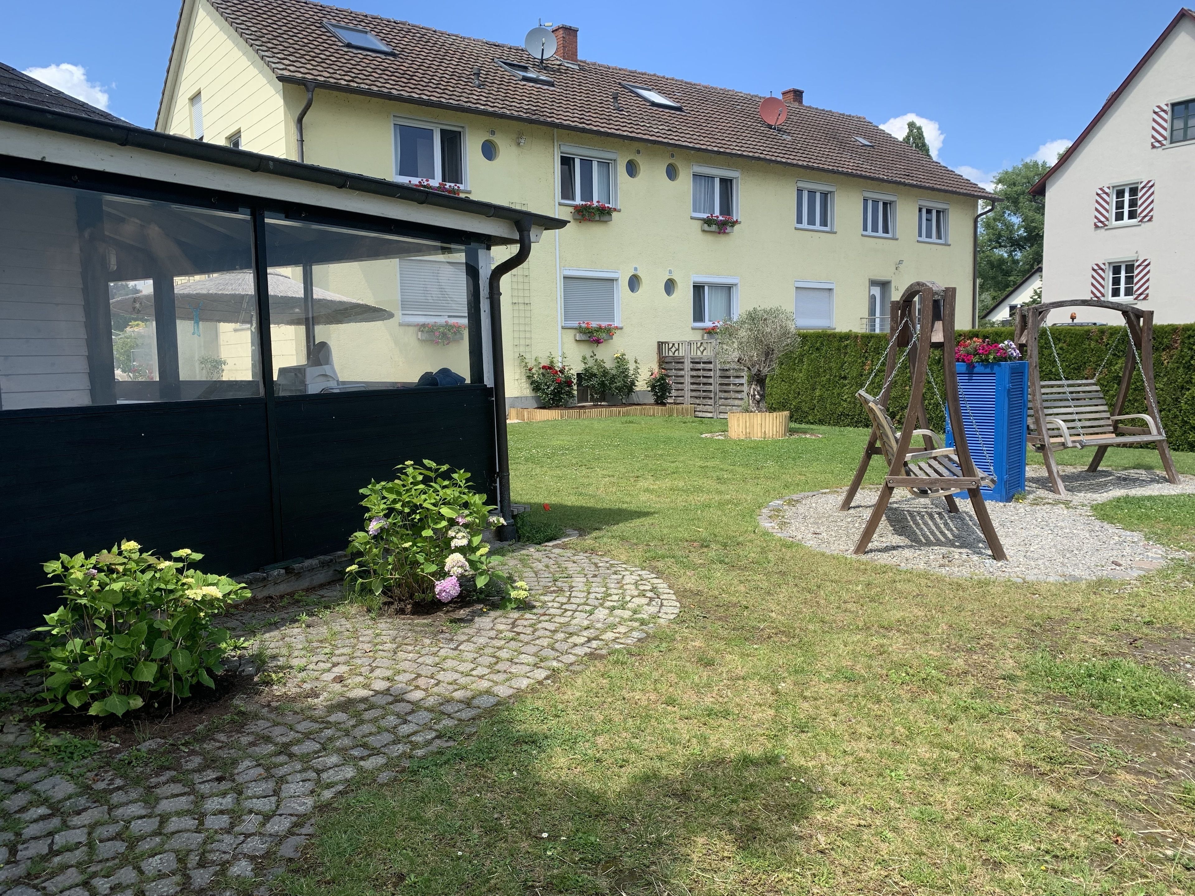 A residential area with a house featuring a covered porch, a swing set, and a garden with potted plants.