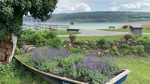 A garden with a wooden boat labeled KN31053, benches, and a view of a lake and bridge. - Gästehaus am See (Gaienhofen)