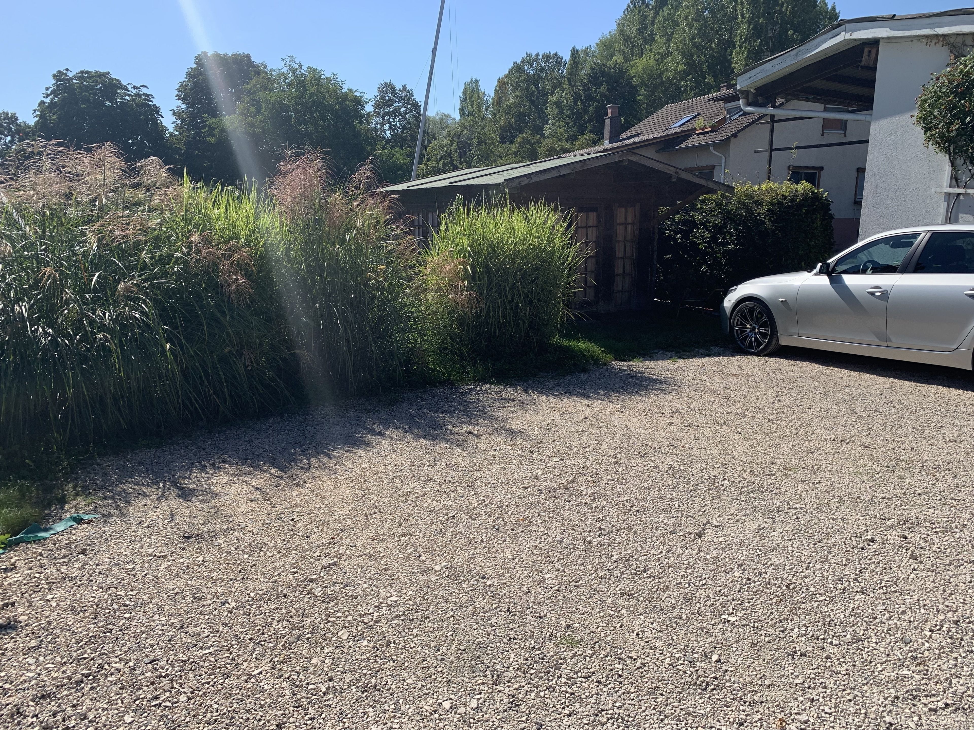 Un camino de grava que lleva a un edificio blanco con techo inclinado, rodeado de vegetación densa y un coche estacionado.