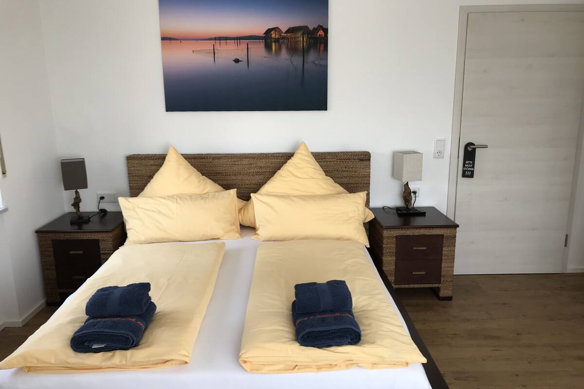 A double bed with two pillows, a bedside table with a lamp, and a painting above the bed.
