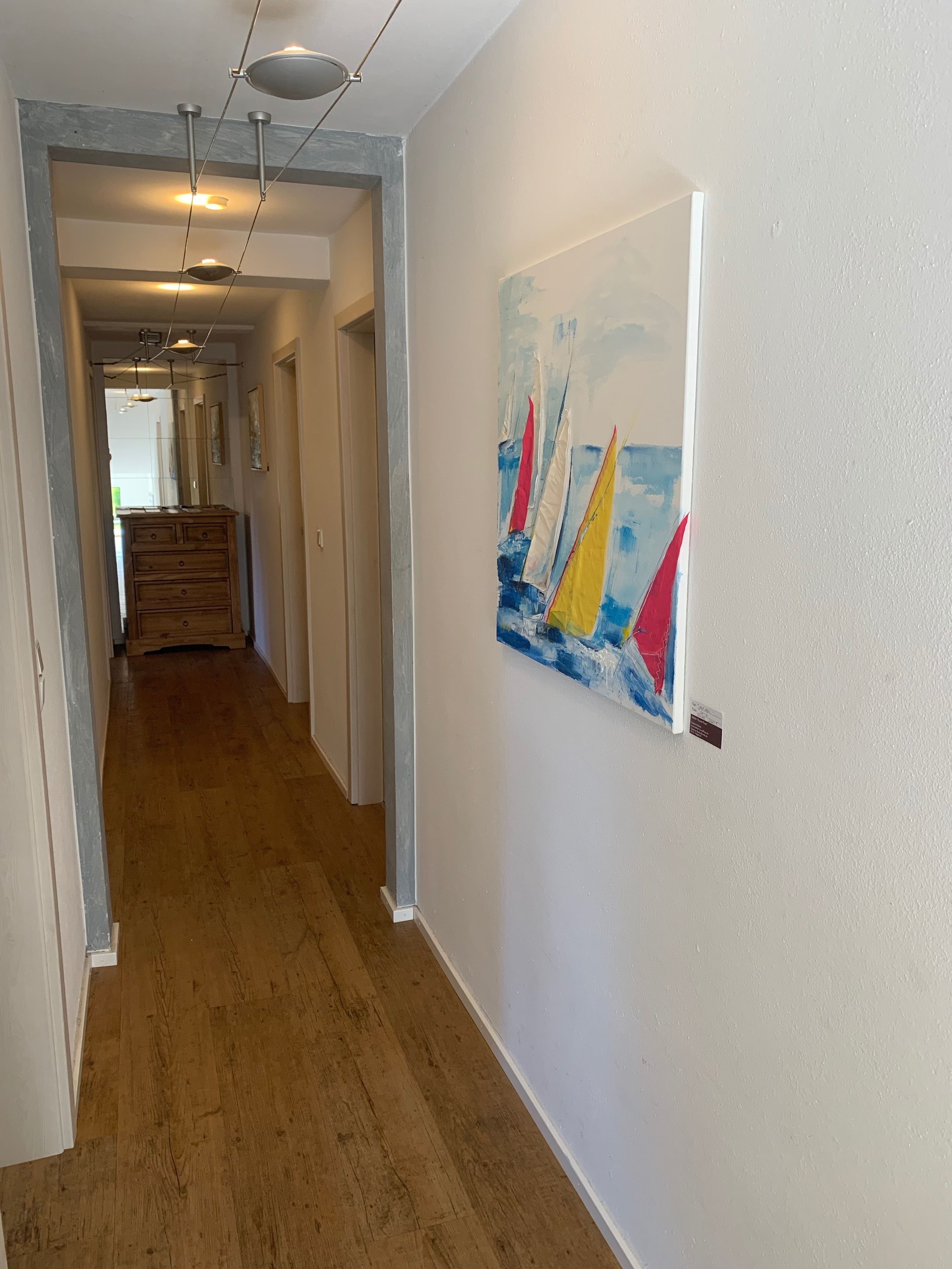 A hallway with wooden flooring, a painting of sailboats on the wall, and a staircase leading to another room.