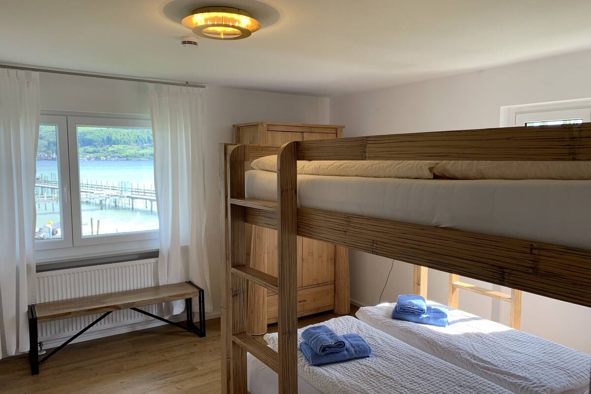 A bunk bed room with a view of a dock and water, a bench, and a ceiling light fixture.