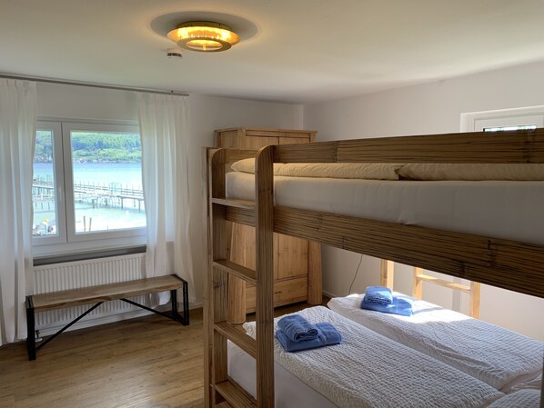Habitación con literas y vista a un muelle y al agua, un banco y una lámpara en el techo.