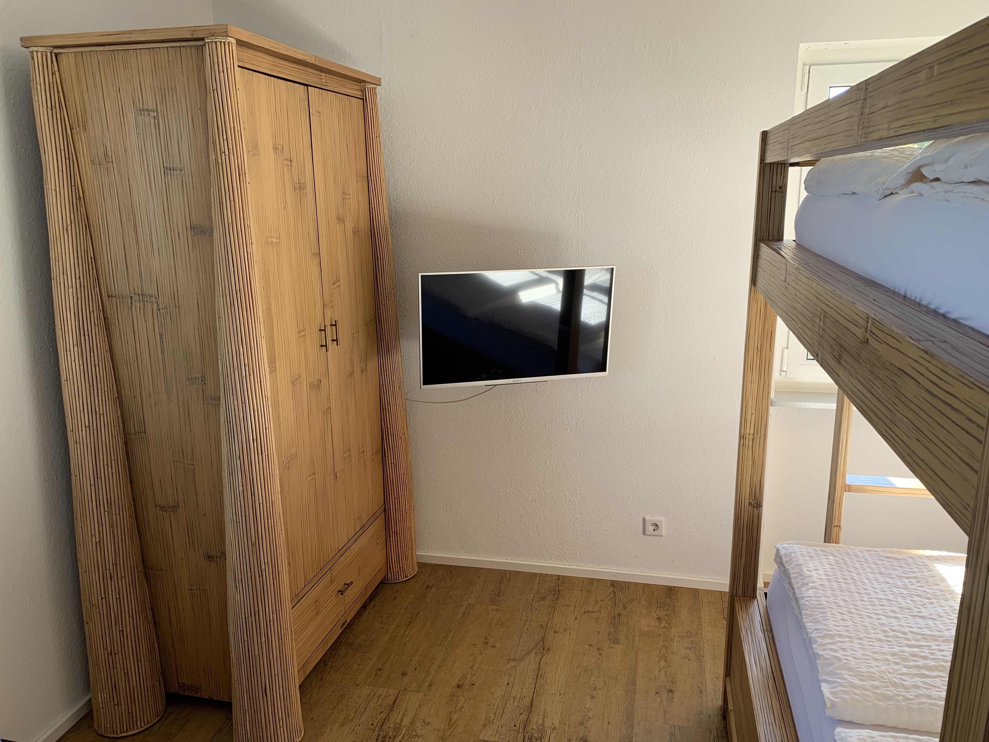 A bedroom with a wooden wardrobe, a mounted TV, and a bunk bed.