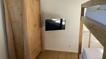 A bedroom with a wooden wardrobe, a mounted TV, and a bunk bed.