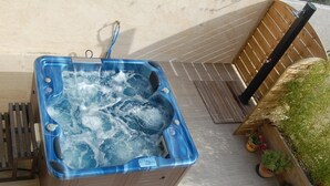 Un jacuzzi con panel de control, rodeado por una terraza de madera y plantas en macetas.
