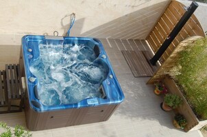 Un jacuzzi con panel de control, rodeado por una terraza de madera y plantas en macetas.